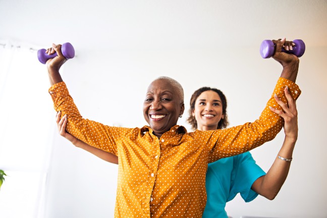 Nurse helping adult with weights exercise